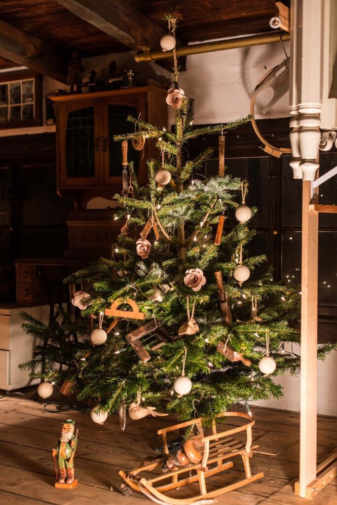 Rustic Christmas tree with vintage tools and wooden ornaments, adorned with warm lights in a cozy room.