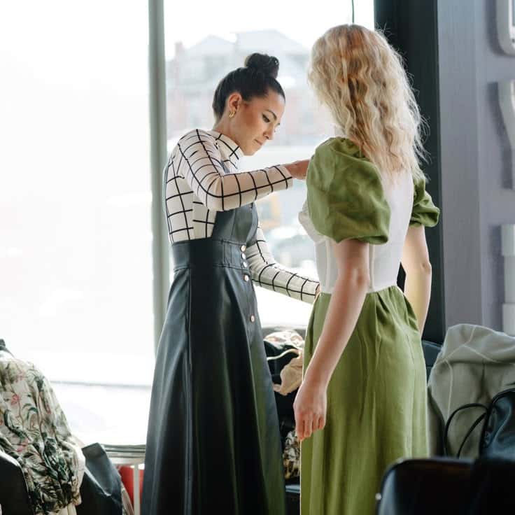 Fashion designer fitting green dress on a model in well-lit studio.
