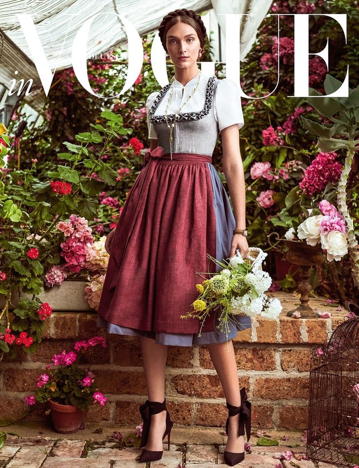 Woman in a traditional dress holding flowers, standing in a garden for a fashion magazine cover shoot.