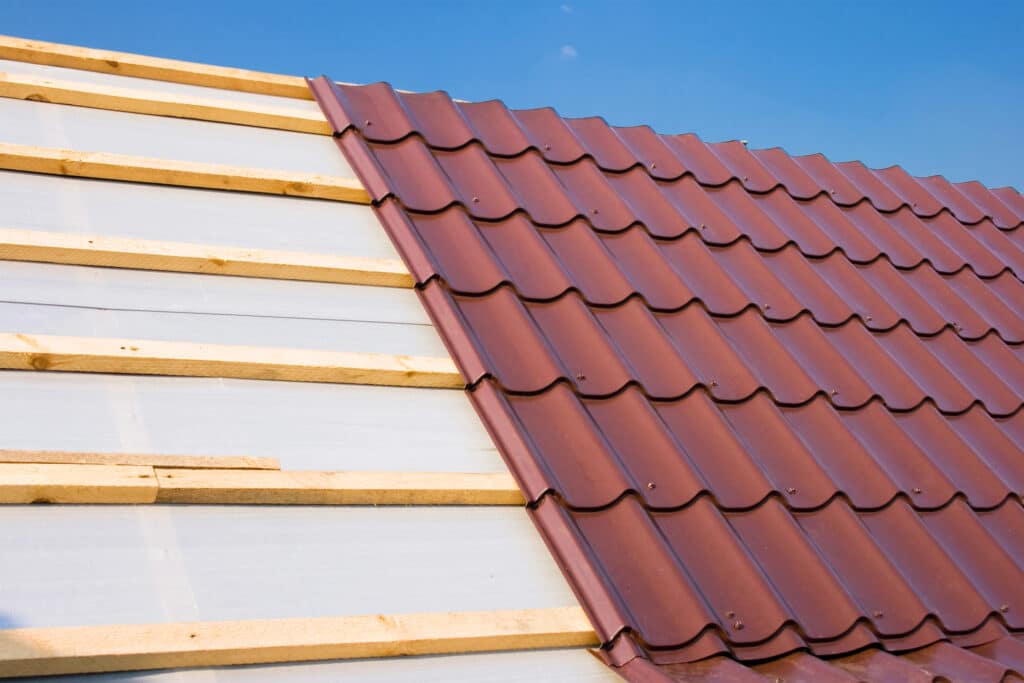 Close-up of metal roof installation with wooden battens against a clear blue sky.