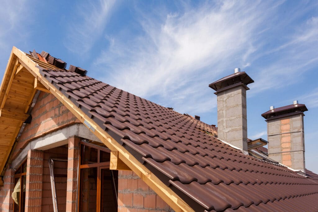 New house under construction with brown tiled roof and two chimneys against a clear blue sky.