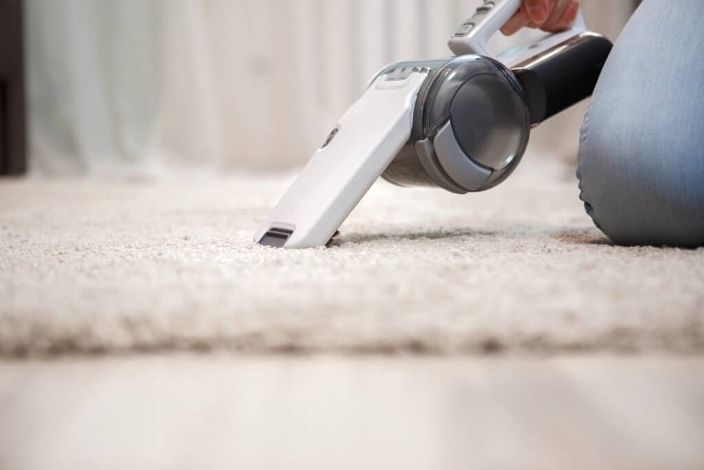 A person using a handheld vacuum cleaner on a beige carpet for effective cleaning.