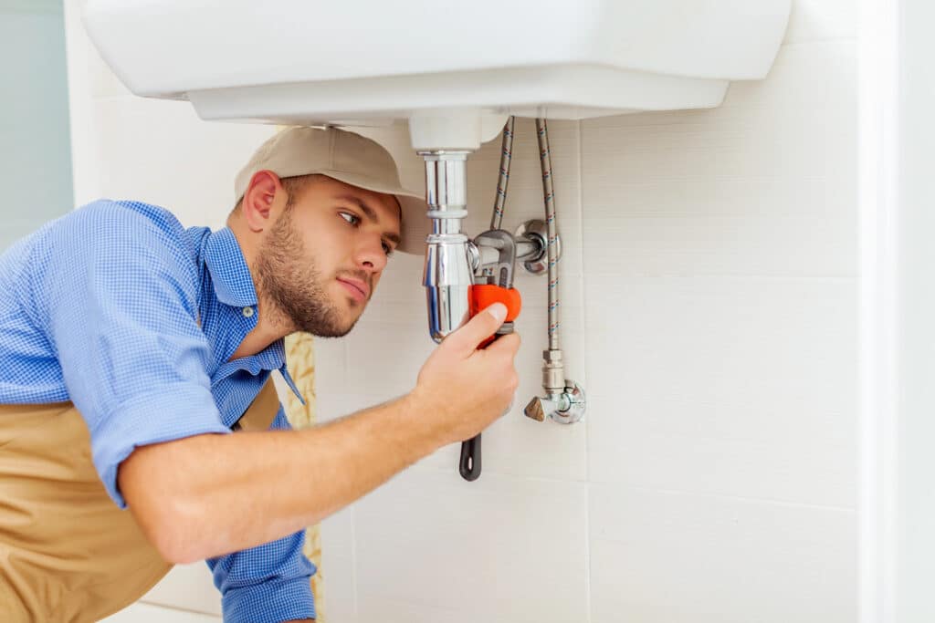 Plumber fixing sink pipe with wrench in bathroom.
