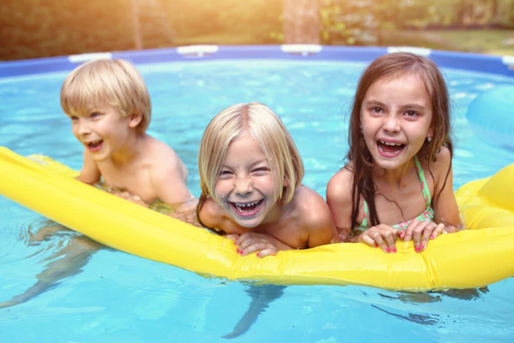 Children laughing and playing in a pool on a sunny day, enjoying water fun with a yellow inflatable float.