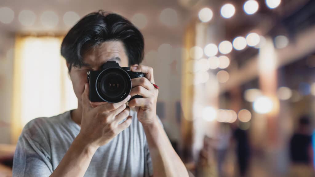 Photographer taking a picture with a DSLR camera in a softly lit indoor setting. Blurred background with lights.
