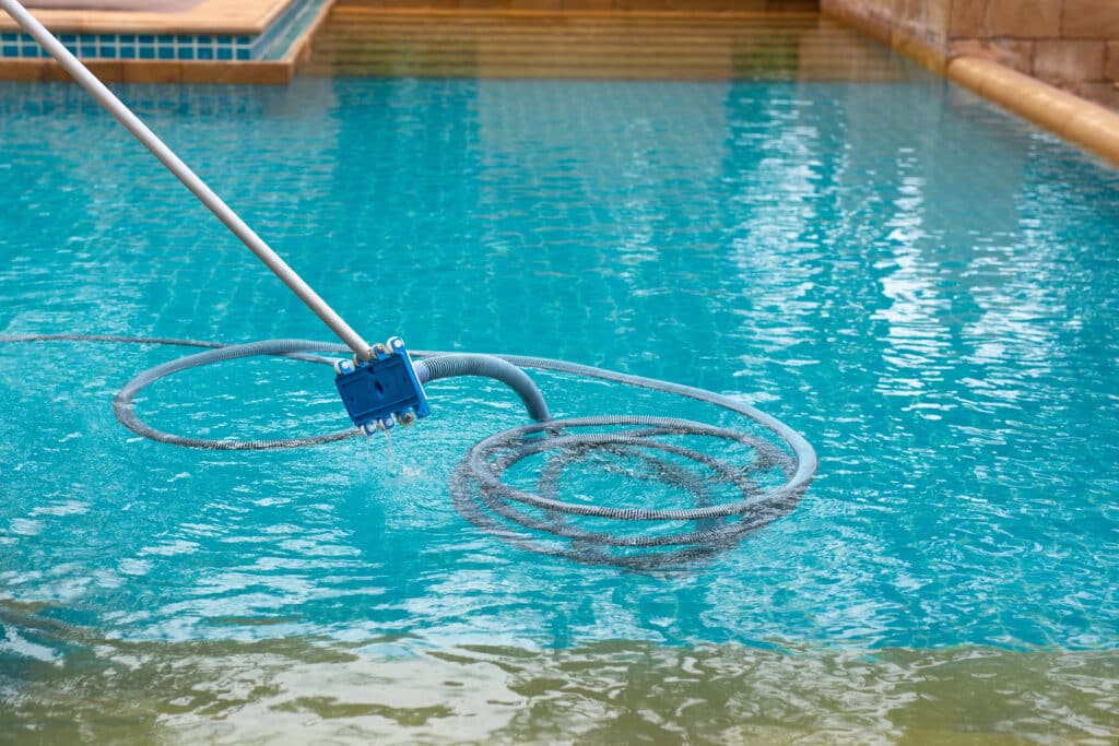 Pool cleaning with a vacuum hose, maintaining clear blue water in a residential swimming pool.