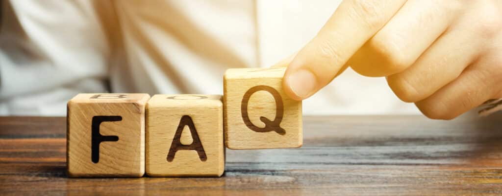 Wooden blocks spelling FAQ with a hand adjusting the Q on a wooden surface.