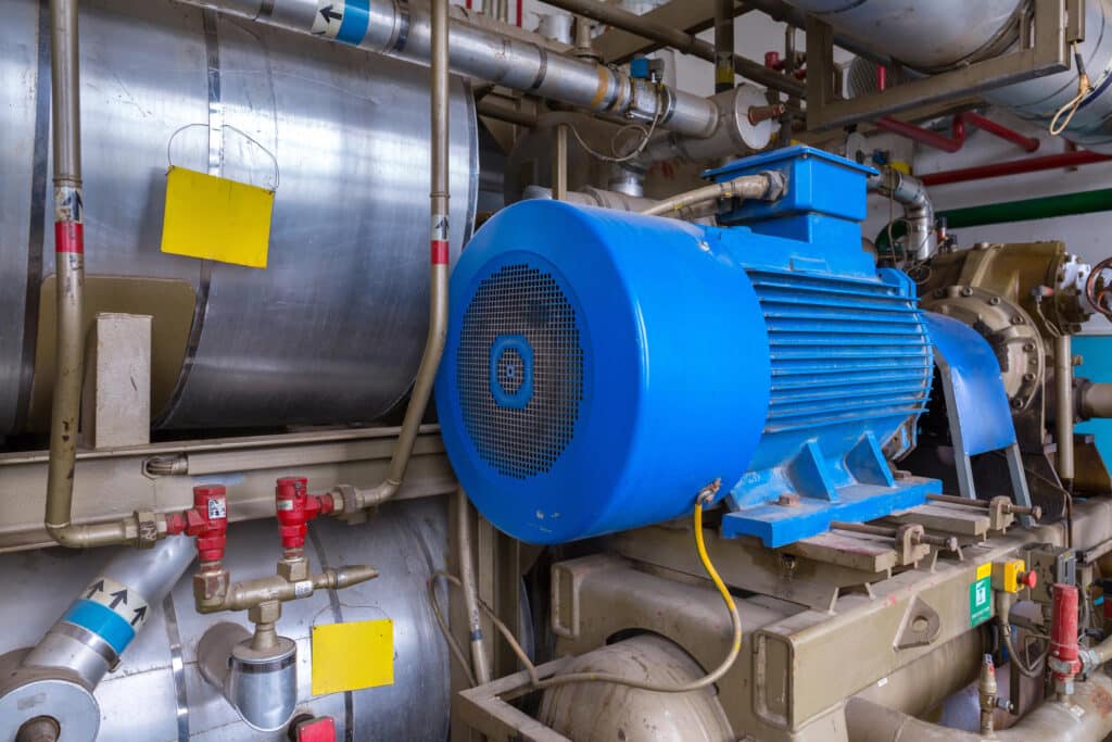 Blue industrial motor and pipes in a machinery room with yellow tags, showcasing engineering infrastructure.
