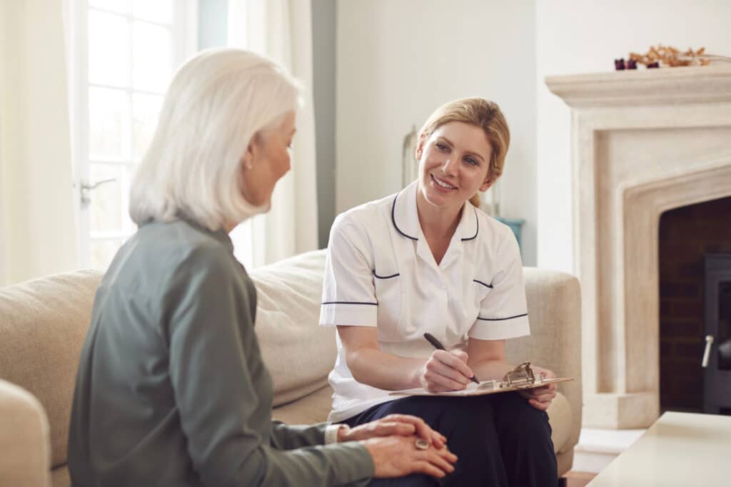 Caregiver chatting with elderly woman in living room, promoting senior care and companionship at home.