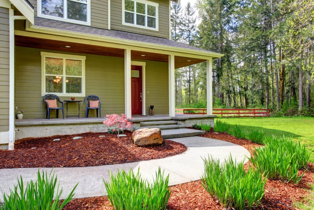 Charming house with inviting porch and lush garden surrounded by tall trees in a peaceful setting.