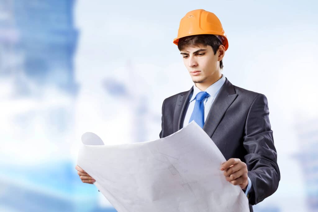 Engineer in a suit and helmet reviewing blueprints at a construction site.
