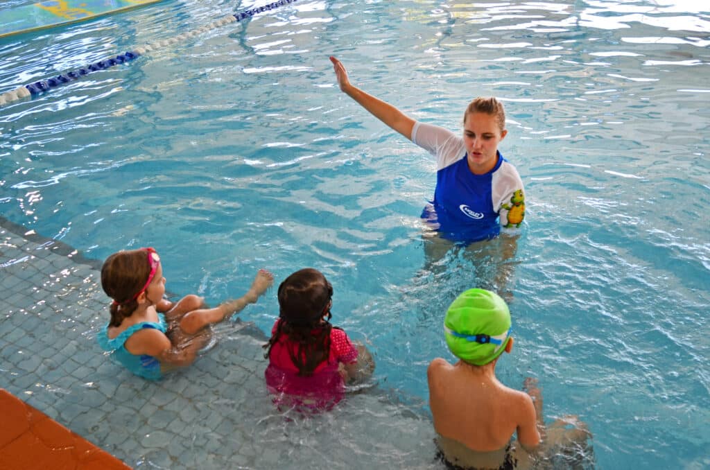 Swimming teacher instructing kids in pool during swim lesson.