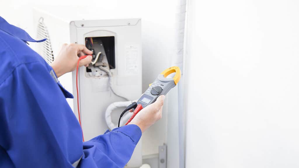 Technician in blue uniform using a digital multimeter to check HVAC system wiring.