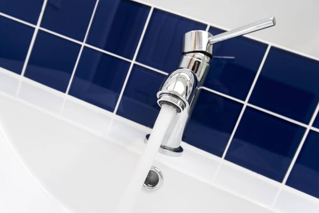 Modern chrome faucet with flowing water in a bathroom with blue tiles.