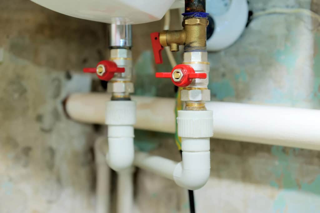 Close-up of plumbing pipes and red valves in a basement setting.