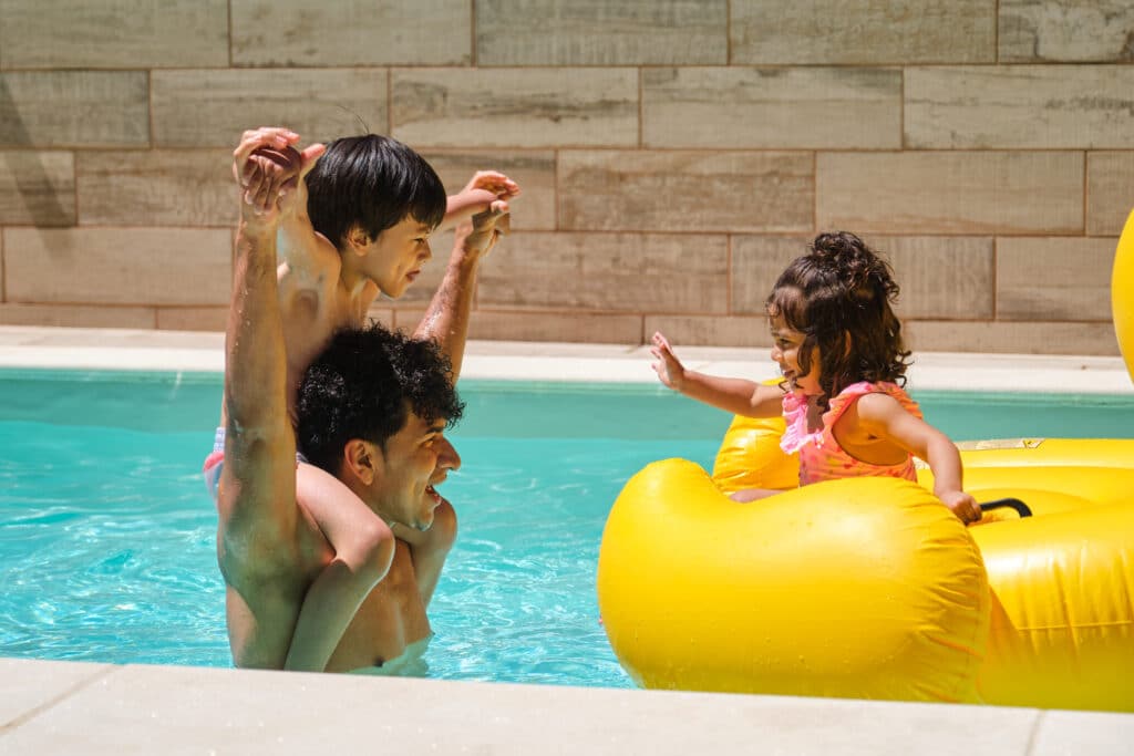 Father and children enjoying a sunny day at the pool with a yellow float.