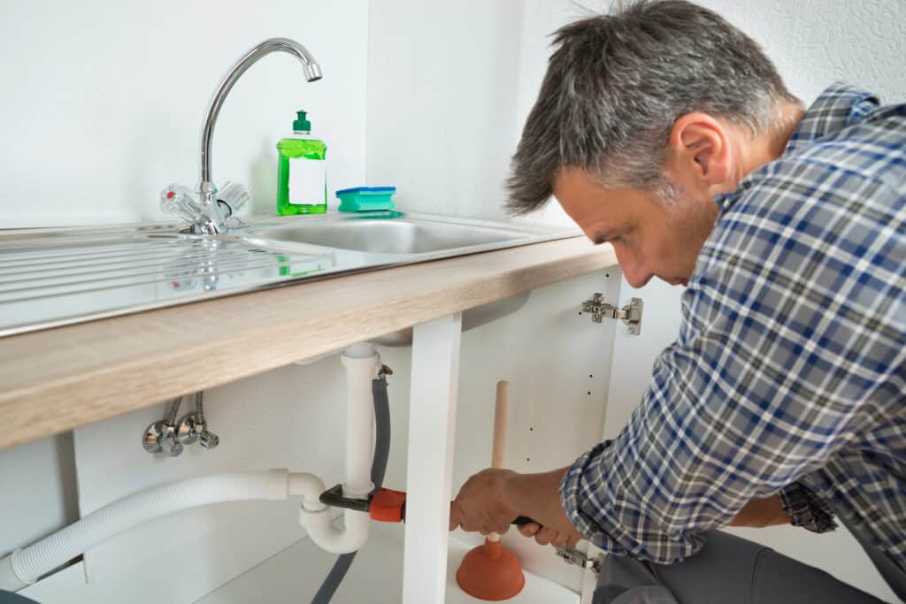 Plumber fixing a kitchen sink pipe with a wrench.