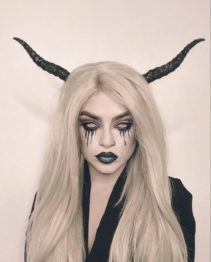 Gothic makeup with dramatic black tears, blonde hair, and horned headpiece for a haunting Halloween look.