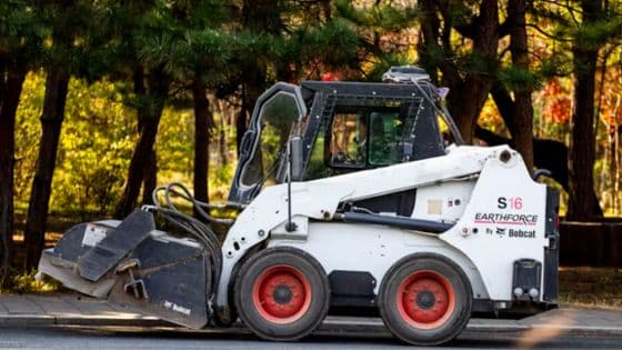 Durability by Design Lessons Automotive Engineers Borrow from Industrial Equipment Skid steer loader on a city street with trees in the background, featuring red wheels and Bobcat branding. | Sky Rye Design Skid steer loader on a city street with trees in the background, featuring red wheels and Bobcat branding.