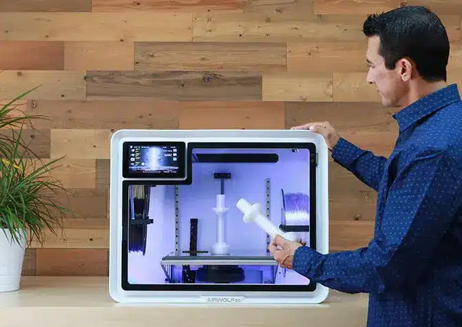 Man demonstrating a 3D printer with a printed object in a modern workspace.