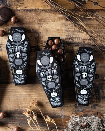 Eight Coffin treat boxes - 7_5_ tall Halloween-themed coffin gift boxes with candy on wooden table, featuring skull designs and festive decorations. | Sky Rye Design Halloween-themed coffin gift boxes with candy on wooden table, featuring skull designs and festive decorations.