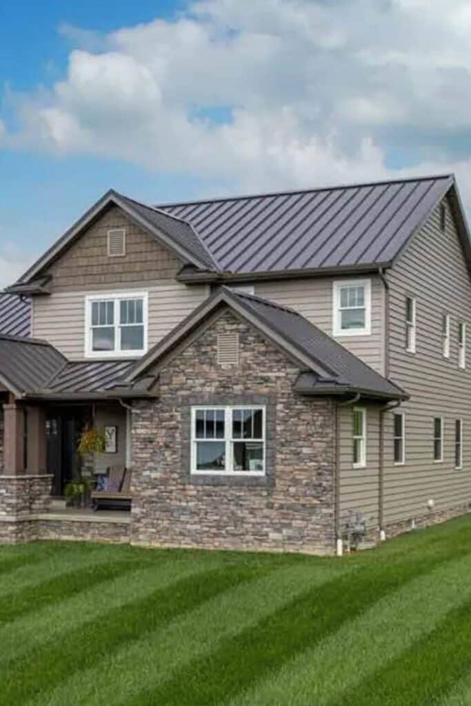 Modern two-story house with stone facade, metal roof, and manicured lawn under a clear blue sky.