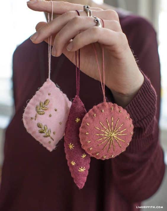 Hand holding three pink handmade felt ornaments with delicate gold embroidery design.