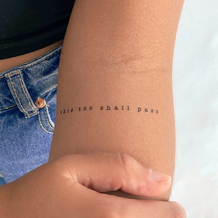 Minimalist arm tattoo reading this too shall pass in typewriter font, close-up view for inspiration and resilience.