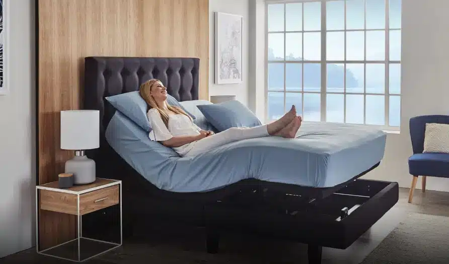 Woman relaxing on adjustable bed with blue sheets in a modern bedroom setting.