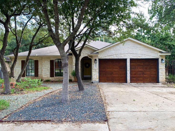 Charming stone house with two-car garage and trees in front yard, perfect for suburban living.