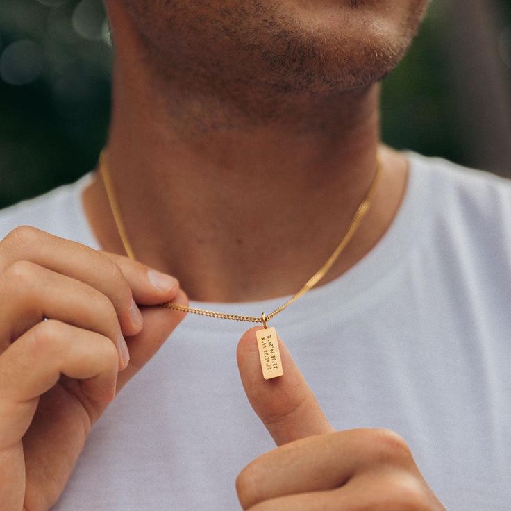 Man wearing a gold necklace with an engraved pendant, close-up, showcasing jewelry detail and style.