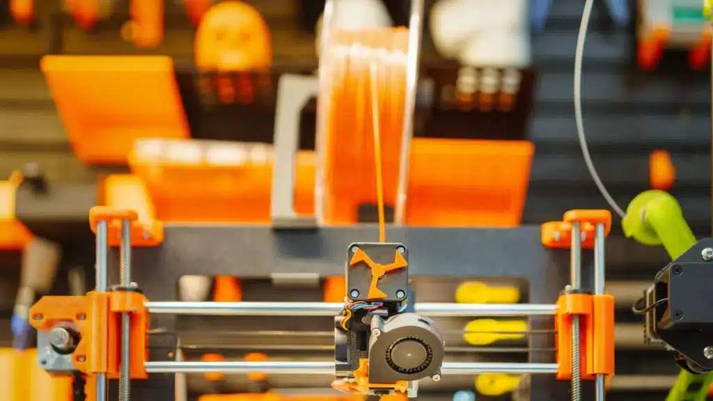 FDM-Printer Close-up of a 3D printer with orange filament in operation, creating precise designs in a modern workshop. | Sky Rye Design Close-up of a 3D printer with orange filament in operation, creating precise designs in a modern workshop.