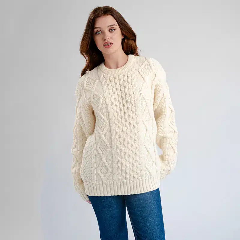 FL194-600-Authentic-Aran-Chunky-Fisherman-Sweater-TaraIrishClothingcom_3_35dd0369-161c-428b-8786-fc31c6b9480c_1024x10242x Woman in cozy cream cable knit sweater and jeans against a neutral background. | Sky Rye Design Woman in cozy cream cable knit sweater and jeans against a neutral background.