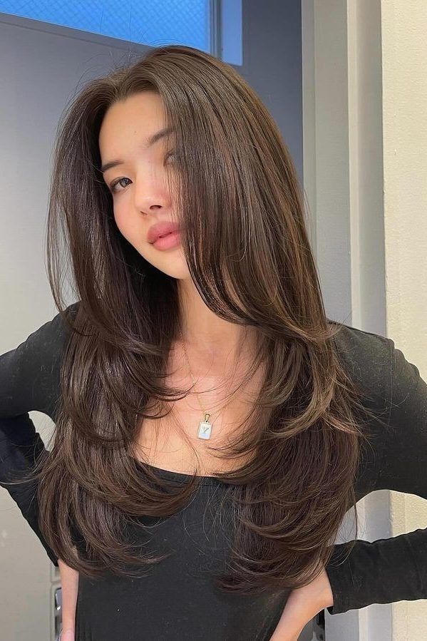 Female with layered brunette hair, wearing a black top, poses confidently indoors.