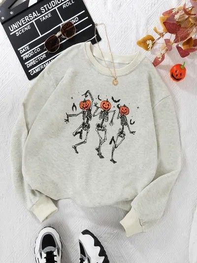 Halloween sweatshirt with dancing skeletons and pumpkin heads, surrounded by autumn leaves and accessories.