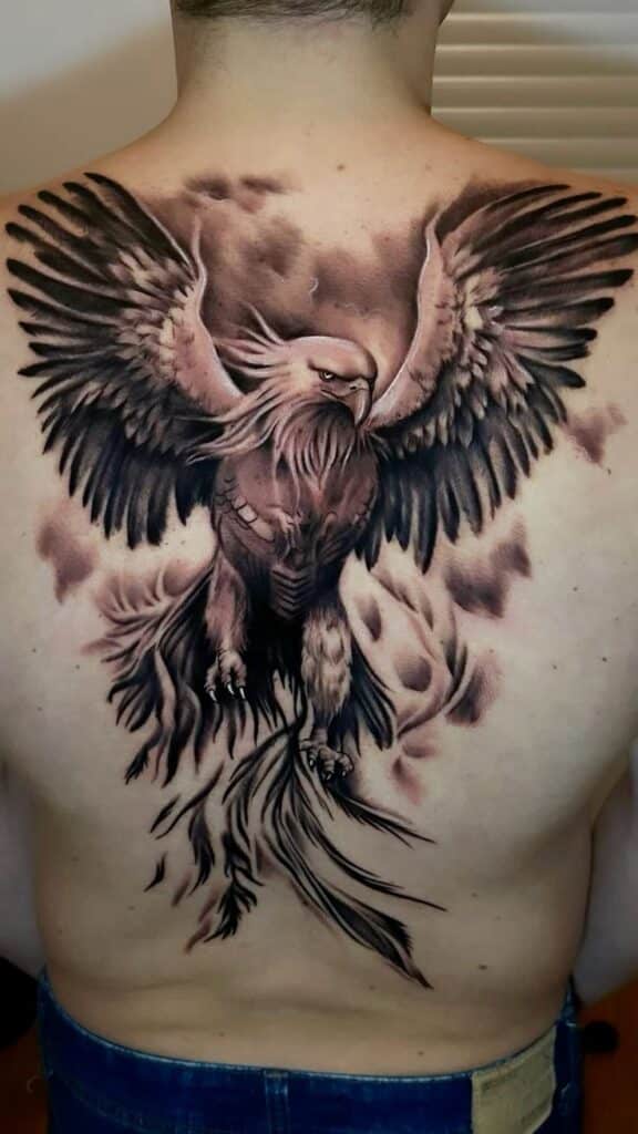 Detailed eagle tattoo on man's back, featuring outstretched wings and fierce expression in grayscale style.