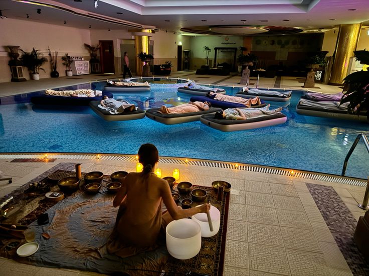 Meditation by a pool with floating beds and calming candles, creating a serene indoor spa ambiance for relaxation.