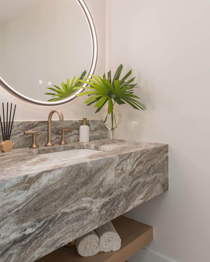 Floating Vanity _ Lindross Remodeling Modern bathroom with round mirror, marble vanity, gold faucet, and green plant accents. Minimalist and elegant design. | Sky Rye Design Modern bathroom with round mirror, marble vanity, gold faucet, and green plant accents. Minimalist and elegant design.