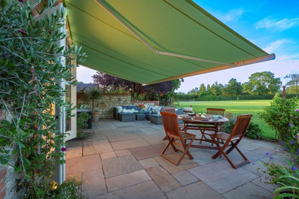 Outdoor patio with awning, wooden furniture, and garden view, ideal for relaxing or dining in a serene setting.