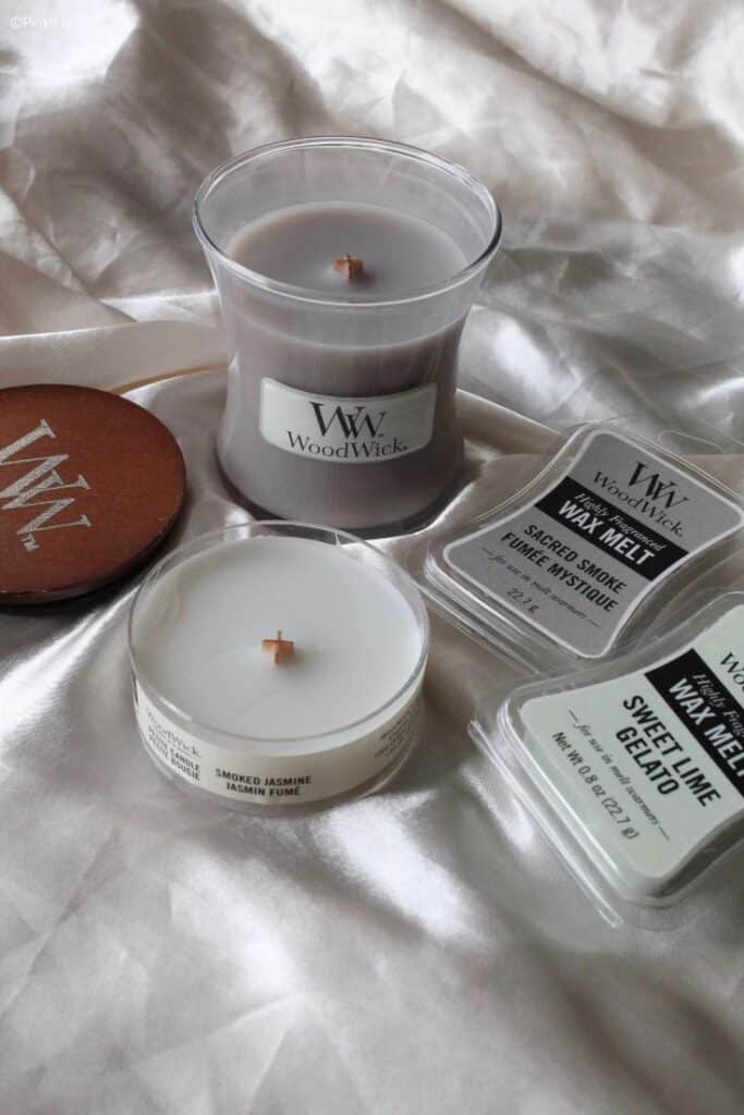Woodwick candle collection on satin fabric, featuring scented candles and wax melts in various fragrances.