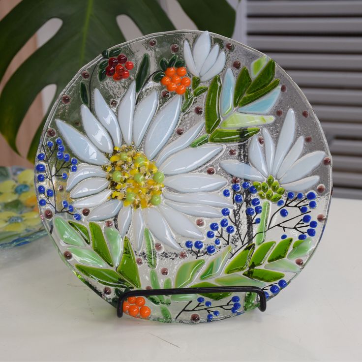 Glass plate with Poppy - Fused glass home decor _ Inspire Uplift Decorative glass plate featuring white daisies and colorful berries, displayed on a table stand. | Sky Rye Design Decorative glass plate featuring white daisies and colorful berries, displayed on a table stand.