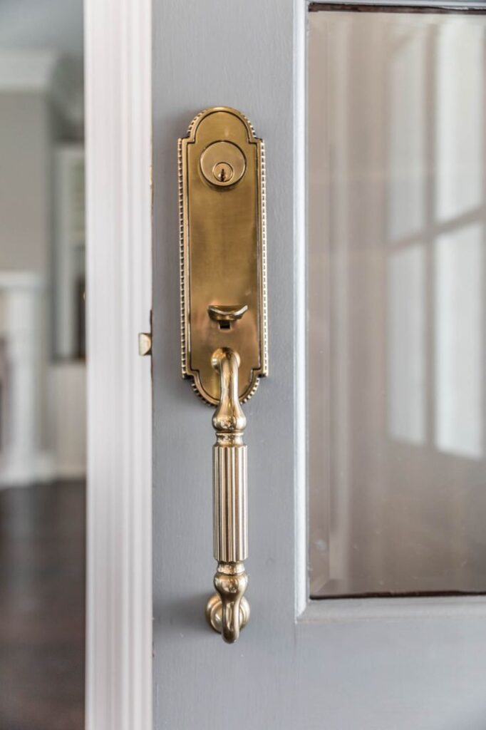 Elegant brass door handle on a gray door with a glass panel, showcasing classic design and polished finish.