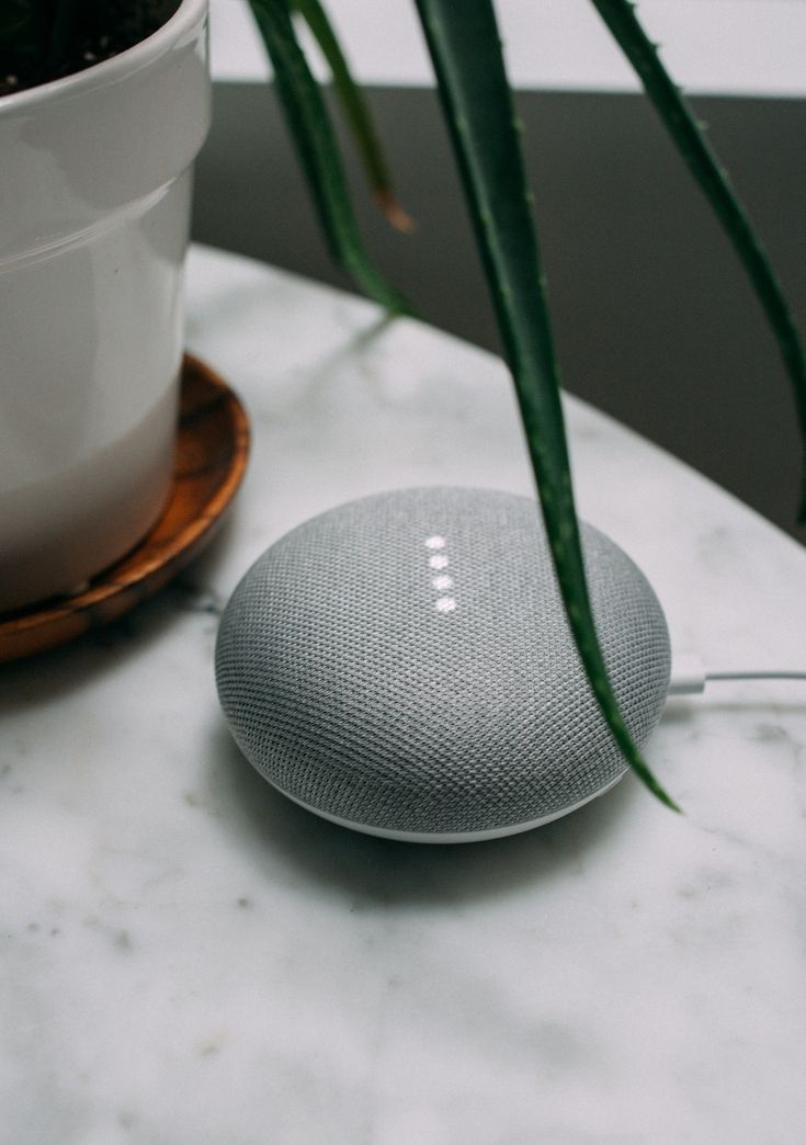 Smart speaker on marble table near potted plant, showcasing modern home tech aesthetics and design.
