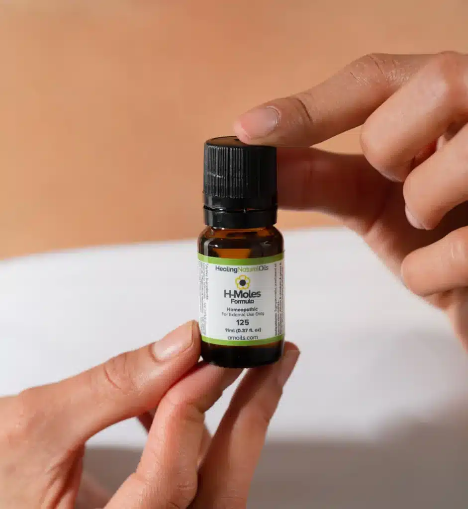Person holding H-Moles Formula essential oil bottle for mole removal.