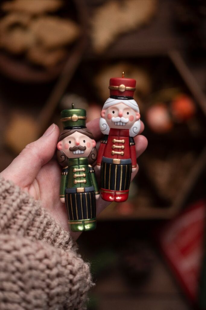 Handmade Christmas Ornament_ Holiday Decor Christmas Tree Ornaments nutcracker Person holding two colorful nutcracker ornaments, one green and one red, perfect for festive holiday decorations. | Sky Rye Design Person holding two colorful nutcracker ornaments, one green and one red, perfect for festive holiday decorations.