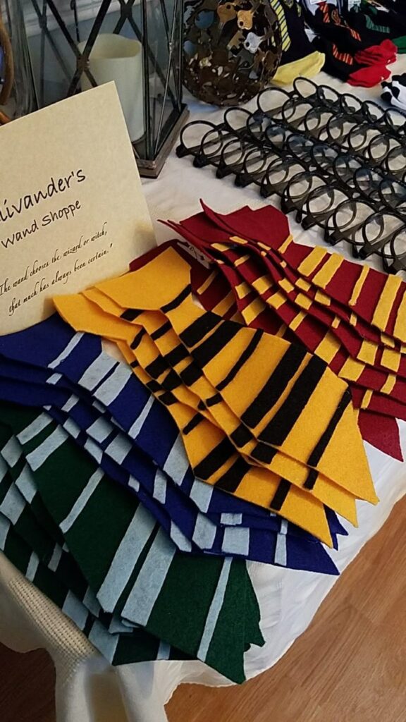 Colorful felt scarves arranged on a table beside decorative glasses and a magical-themed sign.