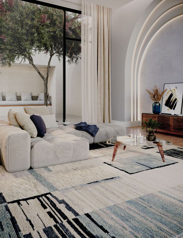 Modern living room with large sofa, abstract rug, and glass coffee table by a window overlooking a garden tree.