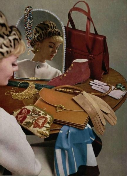 Vintage fashion table with accessories: gloves, handbag, scarf, jewelry, and a woman in leopard hat reflected in mirror.