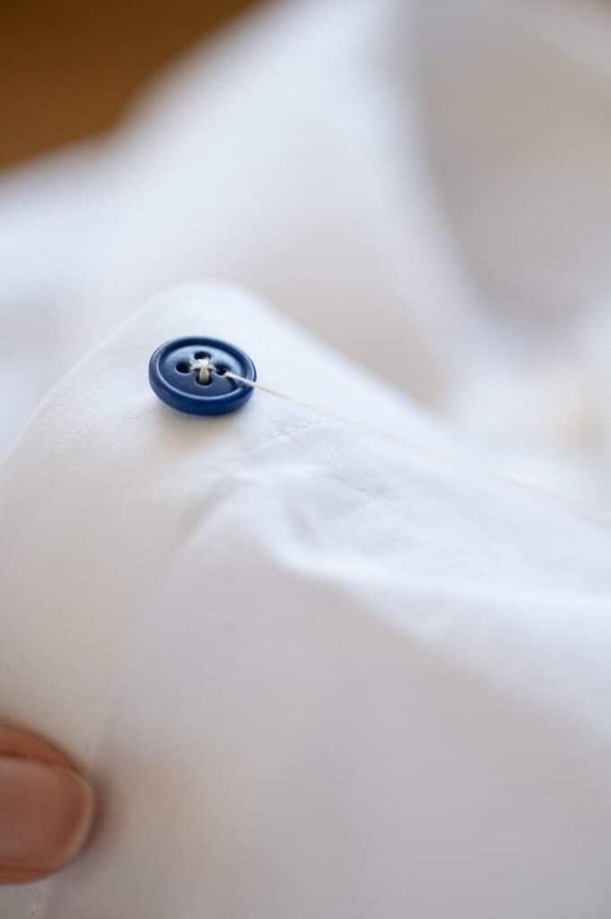 Close-up of blue button on white fabric, sewn with thread. Perfect for sewing or tailoring content.