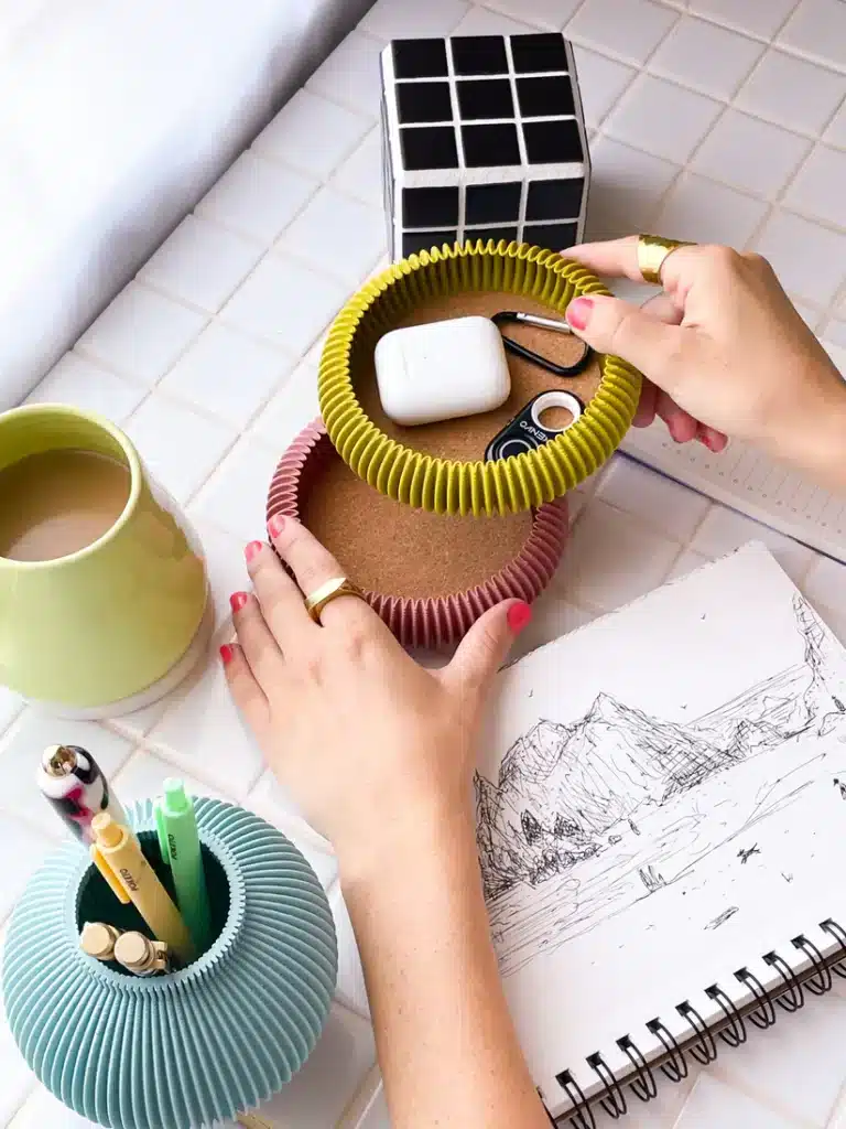 IMG_03592 Hands organizing desktop items, including AirPods, pens, and a sketchbook on a tiled table. | Sky Rye Design Hands organizing desktop items, including AirPods, pens, and a sketchbook on a tiled table.